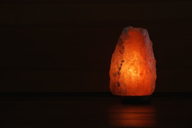 Photo of Himalayan salt lamp glowing on dark background with space for text