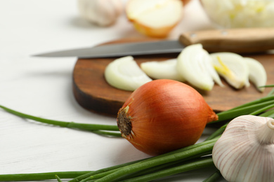 Whole and cut onions on white wooden table, closeup