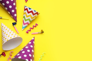Photo of Bright party hats, streamers and horns on yellow background, flat lay. Space for text