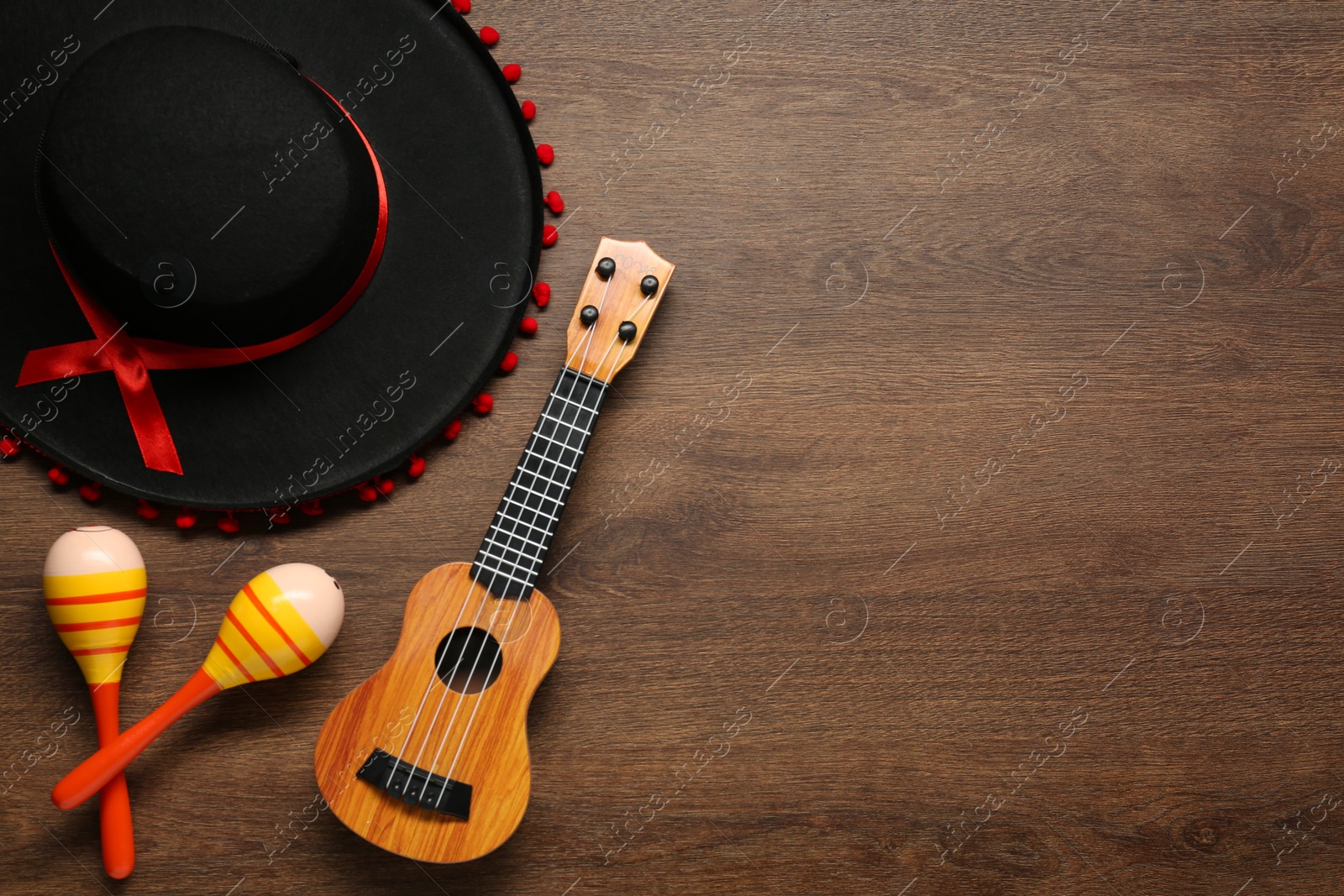 Photo of Mexican sombrero hat, maracas and guitar on wooden background, flat lay. Space for text