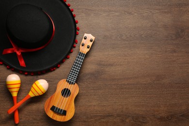 Photo of Mexican sombrero hat, maracas and guitar on wooden background, flat lay. Space for text