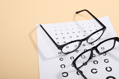 Vision test chart and glasses on beige background, space for text