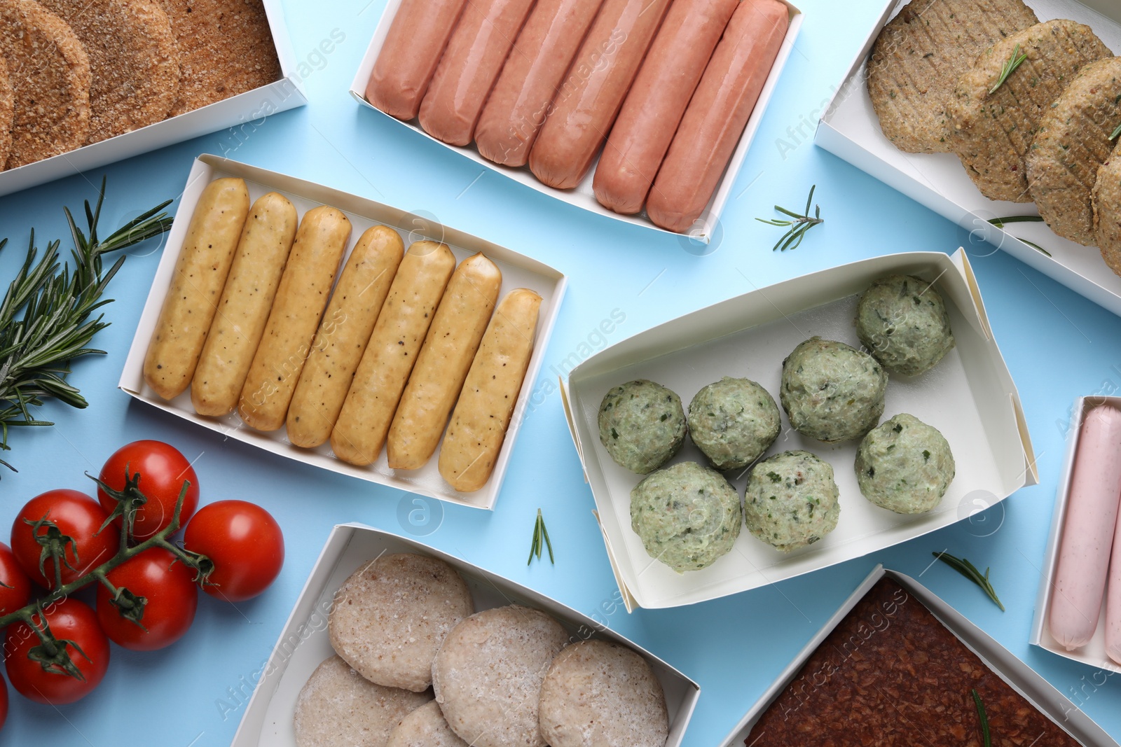 Photo of Many different raw vegan meat products, rosemary and tomatoes on light blue background, flat lay