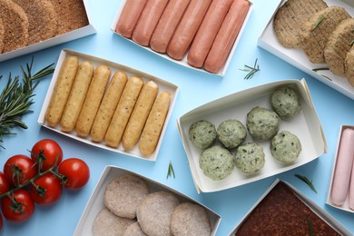 Photo of Many different raw vegan meat products, rosemary and tomatoes on light blue background, flat lay