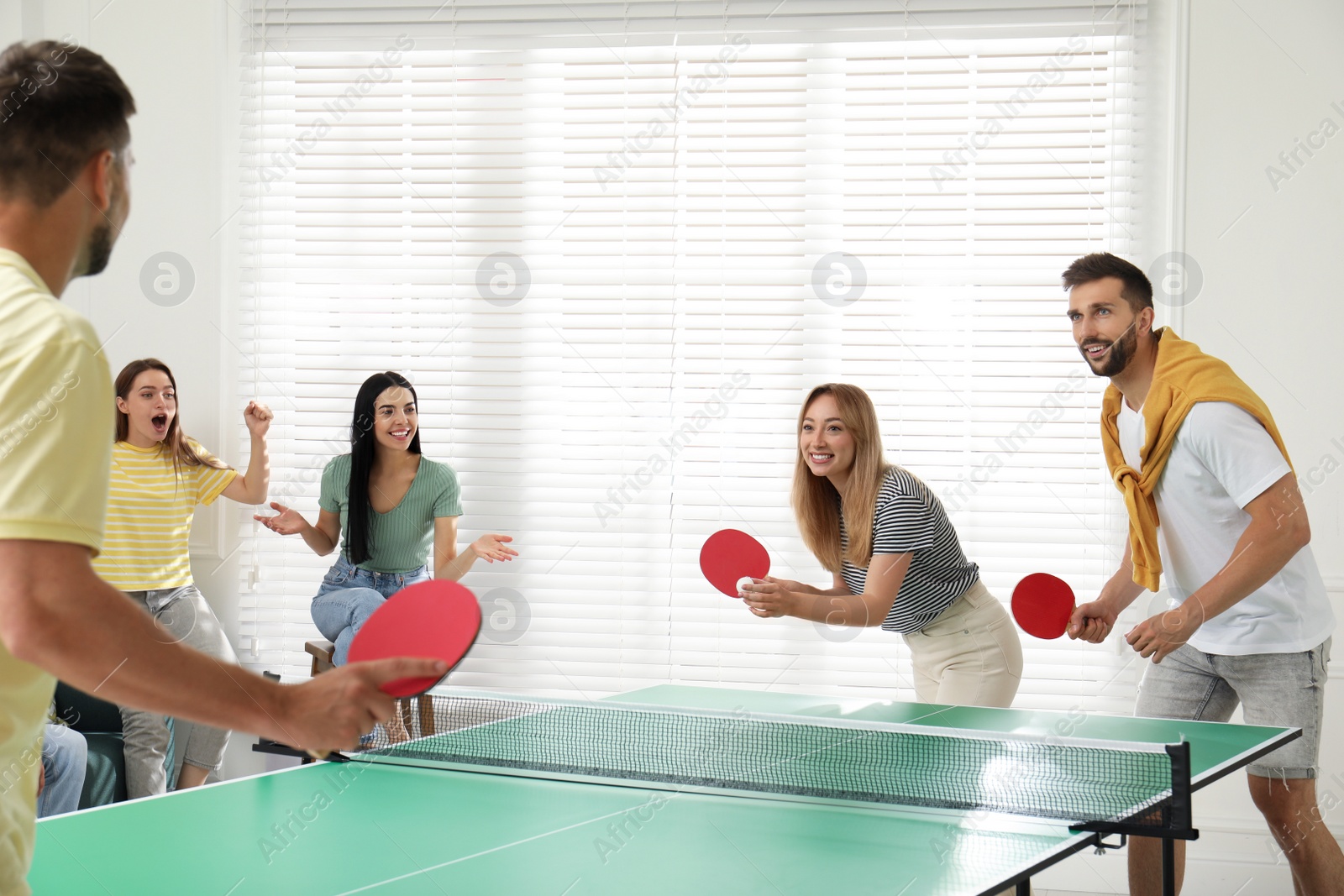 Photo of Happy friends playing ping pong together indoors