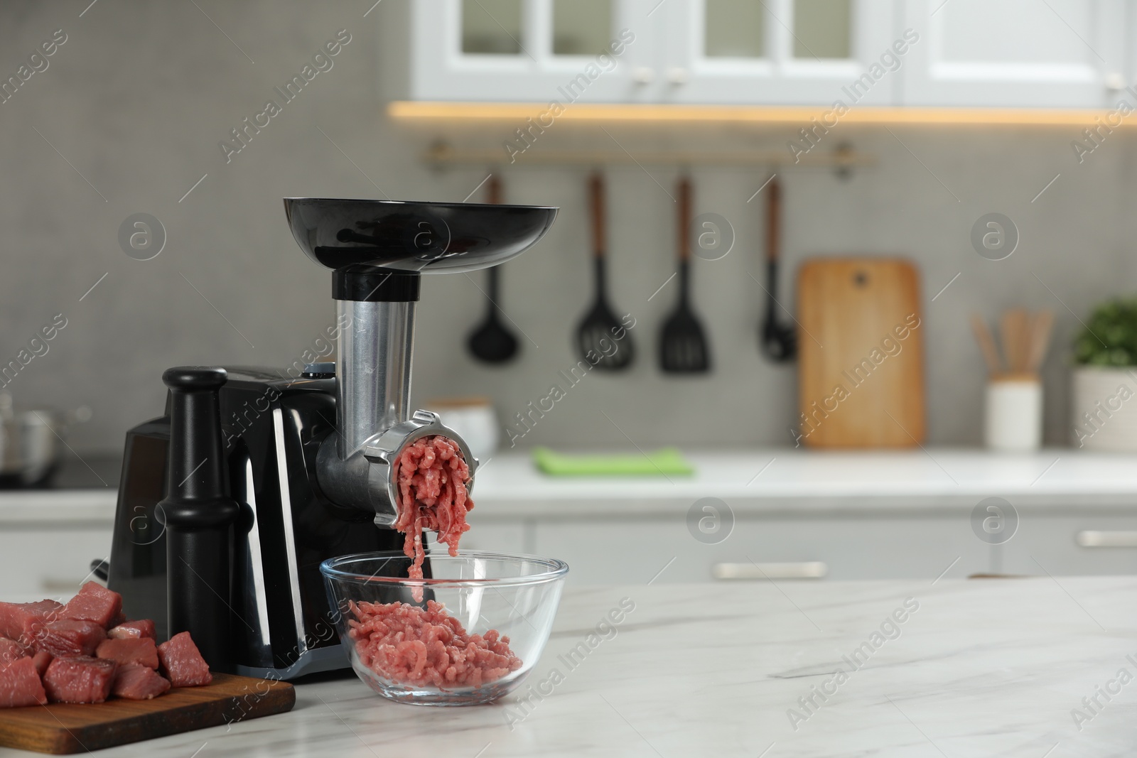 Photo of Electric meat grinder with beef mince on white table in kitchen, space for text