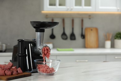 Electric meat grinder with beef mince on white table in kitchen, space for text