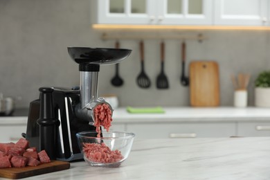 Photo of Electric meat grinder with beef mince on white table in kitchen, space for text