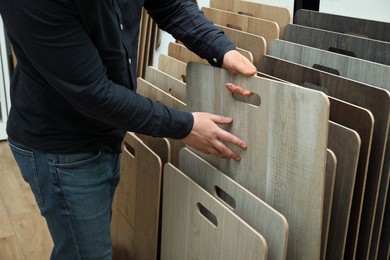 Photo of Man choosing wooden flooring among different samples in shop, closeup