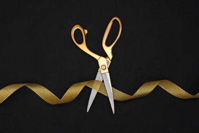 Gold satin ribbon and scissors on black background, flat lay