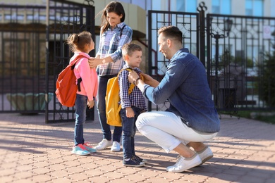 Young parents saying goodbye to their little children near school