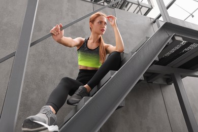 Beautiful woman in stylish gym clothes sitting on stairs on street, low angle view