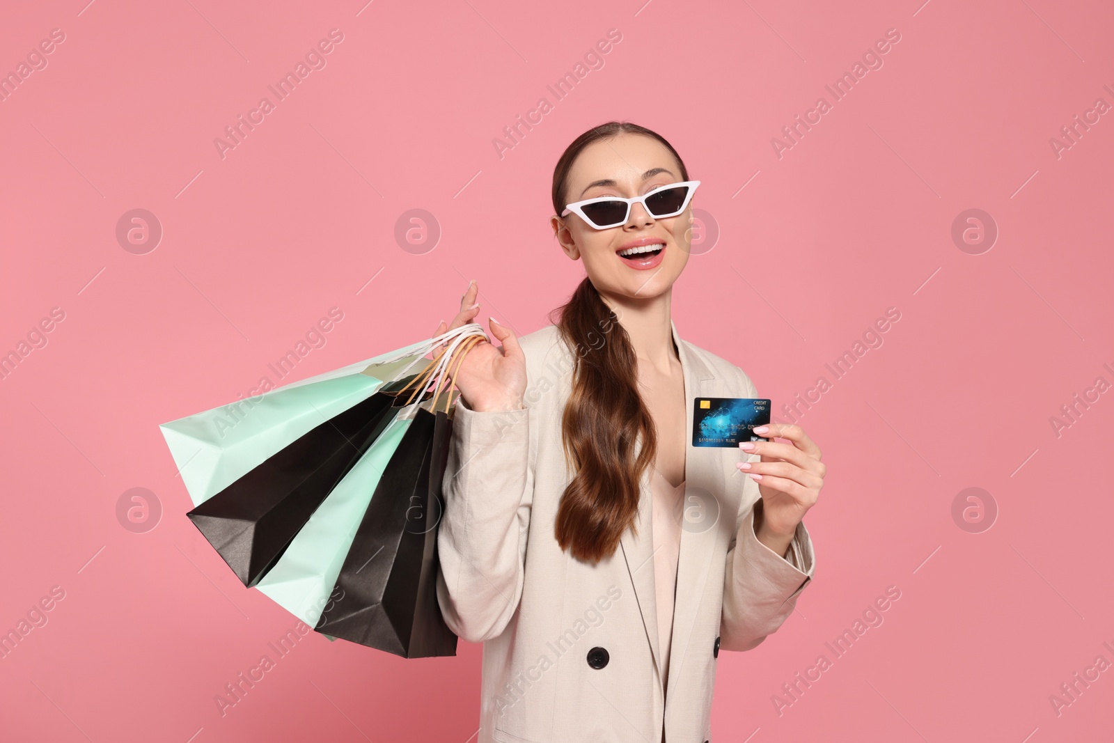 Photo of Stylish young woman with shopping bags and credit card on pink background