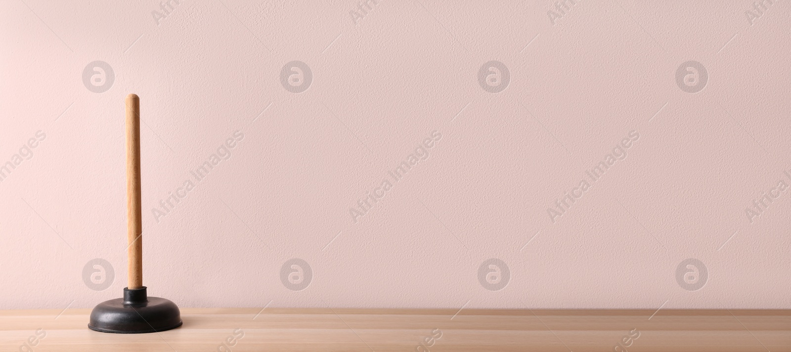 Photo of Plunger on wooden table against pink background. Space for text