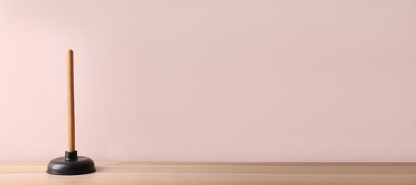 Plunger on wooden table against pink background. Space for text