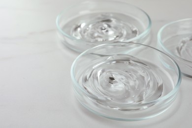 Photo of Petri dishes with liquids on white marble table, closeup. Space for text