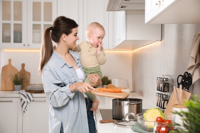 Photo of Happy young woman holding her cute little baby while cooking in kitchen