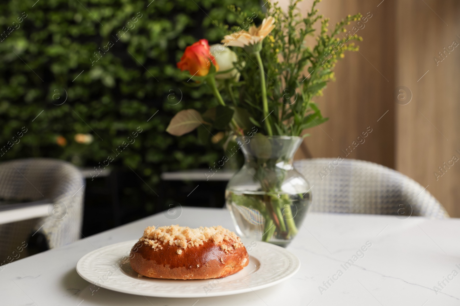 Photo of Tasty bun and vase with flowers on table in cafeteria