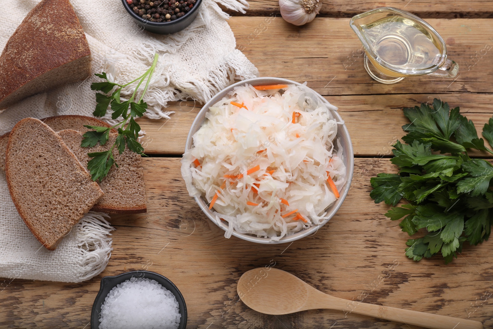 Photo of Bowl of tasty sauerkraut and ingredients on wooden table, flat lay