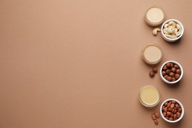 Different types of delicious nut butters and ingredients on brown background, flat lay. Space for text