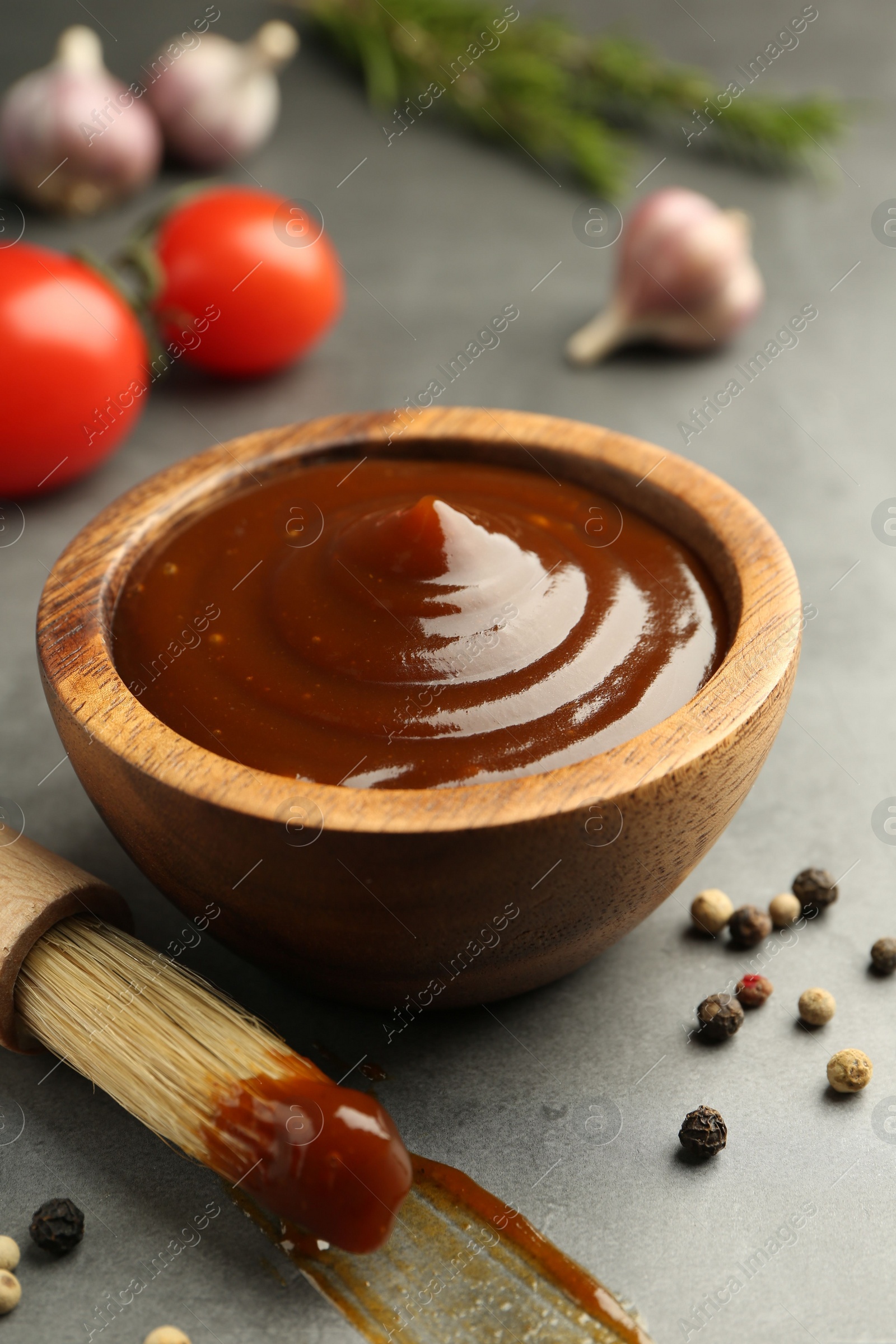 Photo of Tasty barbeque sauce in bowl, brush and peppercorns on grey table, closeup