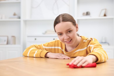 Woman cleaning wooden table with rag indoors