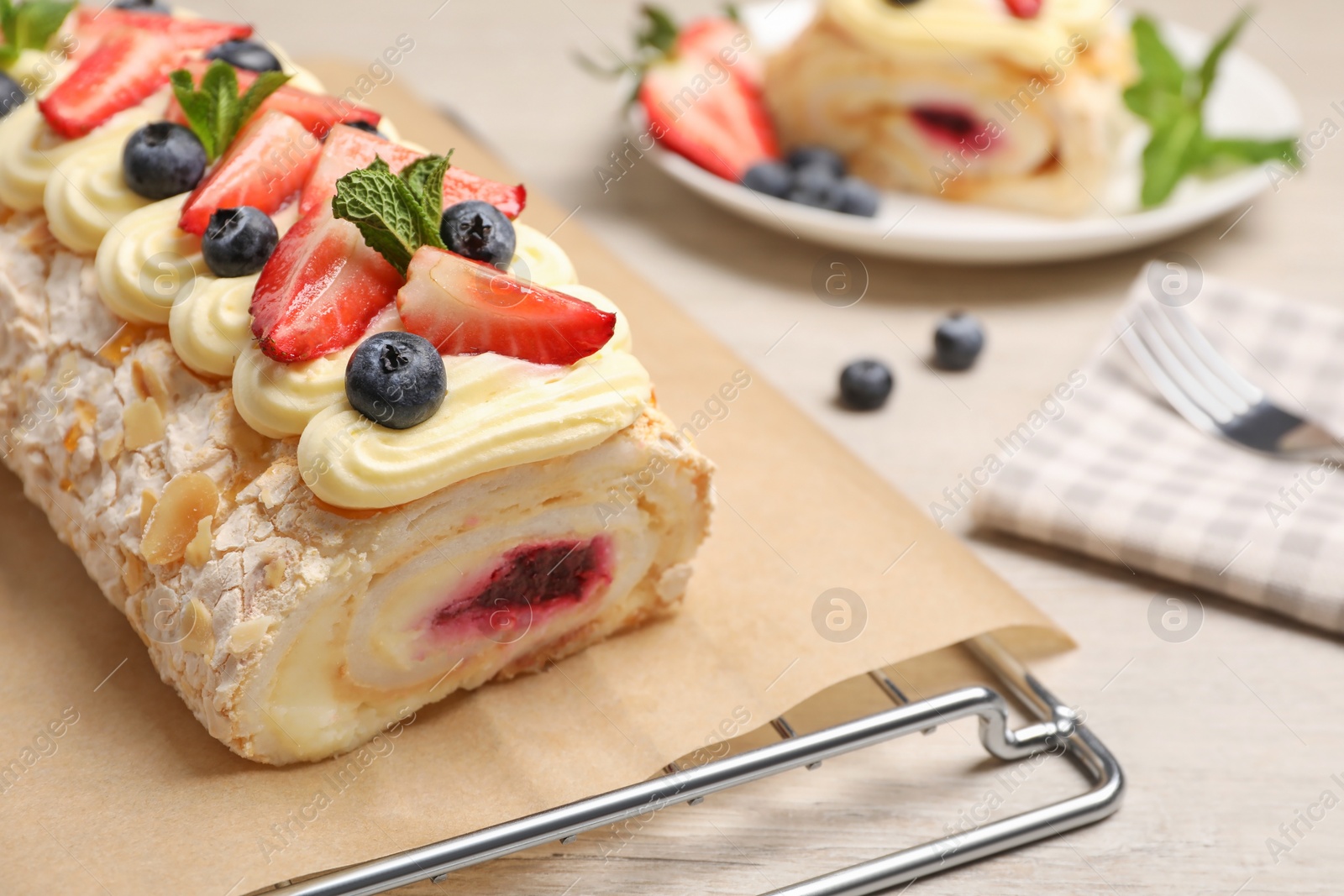 Photo of Tasty meringue roll with jam, cream, strawberry, blueberry and mint on white wooden table, closeup. Space for text