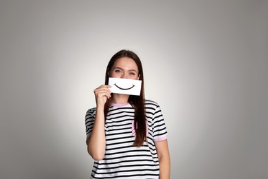 Woman holding sheet of paper with smile on grey background