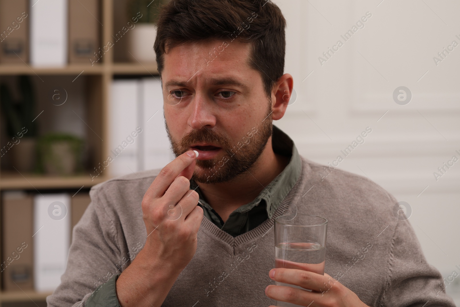 Photo of Depressed man with glass of water taking antidepressant pill on blurred background