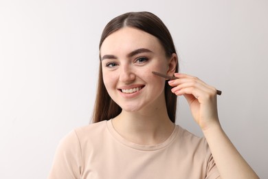 Smiling woman drawing freckles with pen on light background