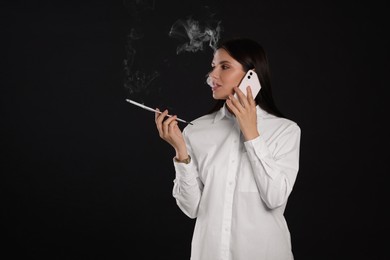 Photo of Woman using long cigarette holder for smoking while talking on phone against black background, space for text