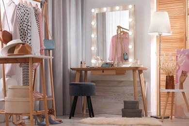 Photo of Makeup room. Stylish dressing table with mirror, chair and clothes rack indoors