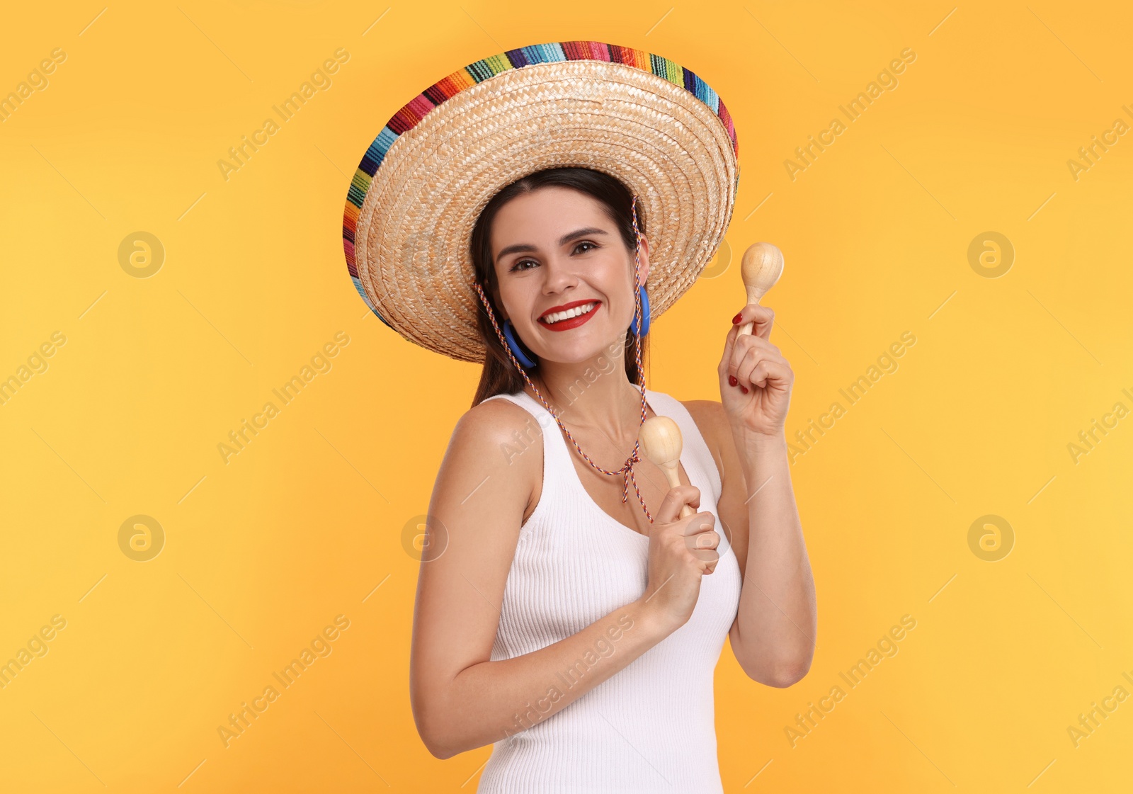 Photo of Young woman in Mexican sombrero hat dancing with maracas on yellow background