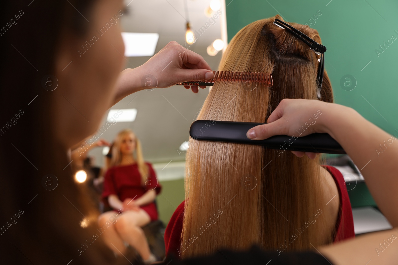 Photo of Stylist straightening woman's hair with flat iron in salon