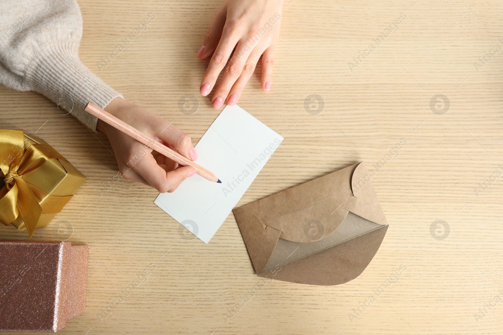 Photo of Woman writing message in greeting card on wooden table, top view