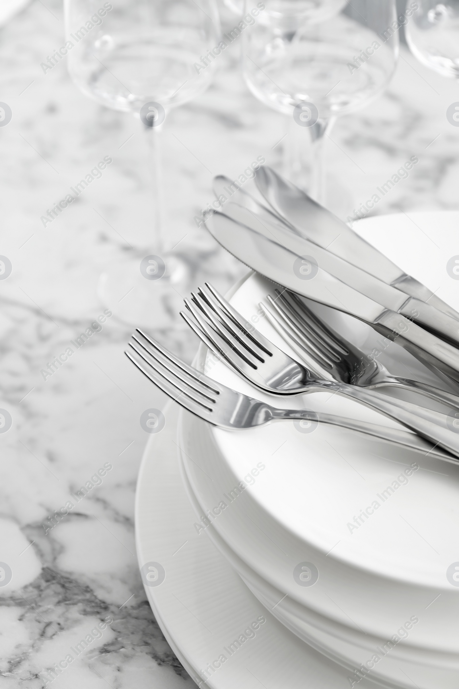 Photo of Plates with knives forks on white marble table, closeup