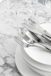 Plates with knives forks on white marble table, closeup