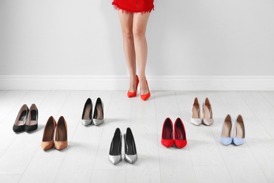 Woman trying on different high heel shoes near light wall, closeup