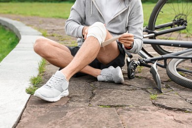 Man applying bandage onto his knee near bicycle outdoors, closeup