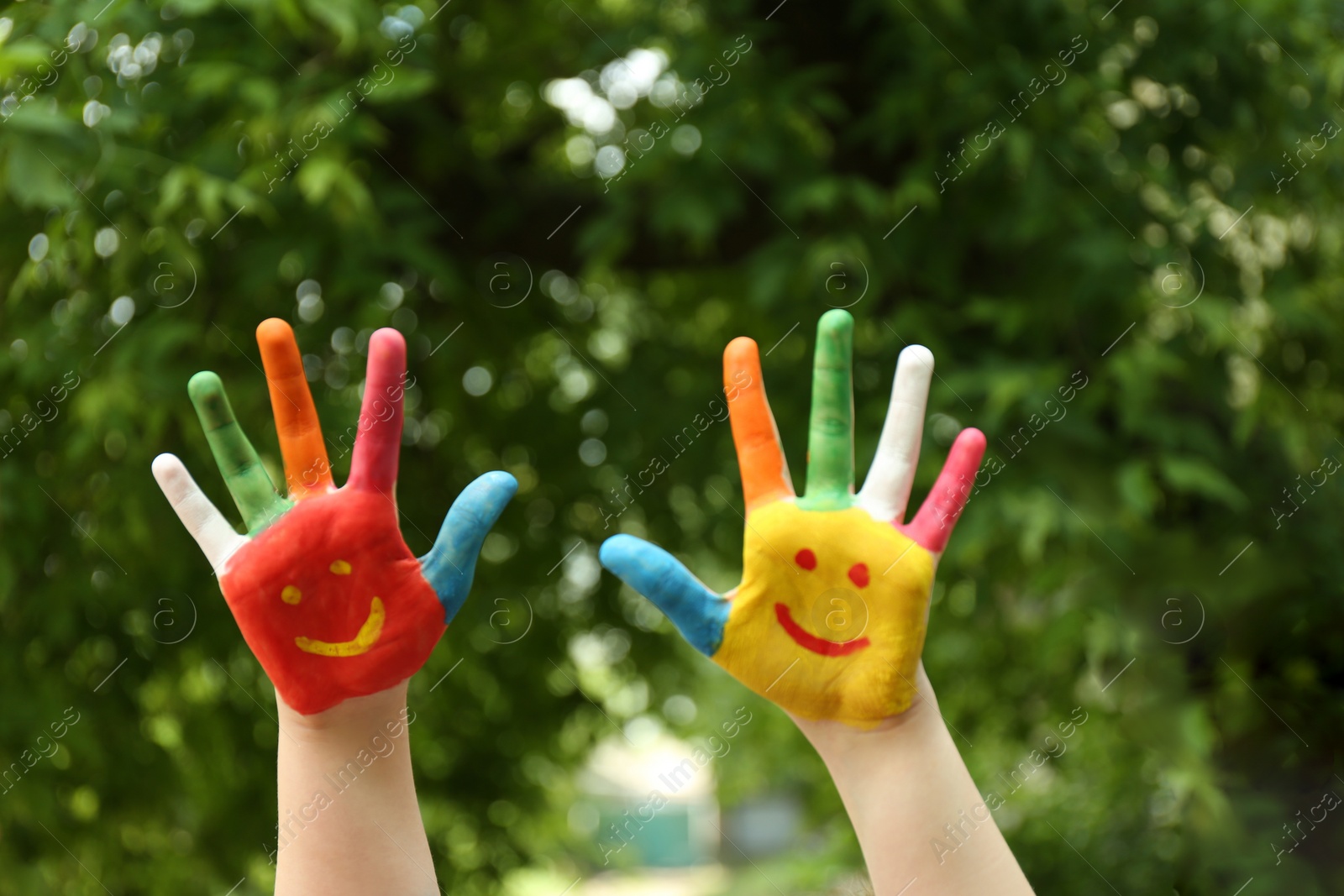 Photo of Kid with smiling faces drawn on palms in green park, closeup