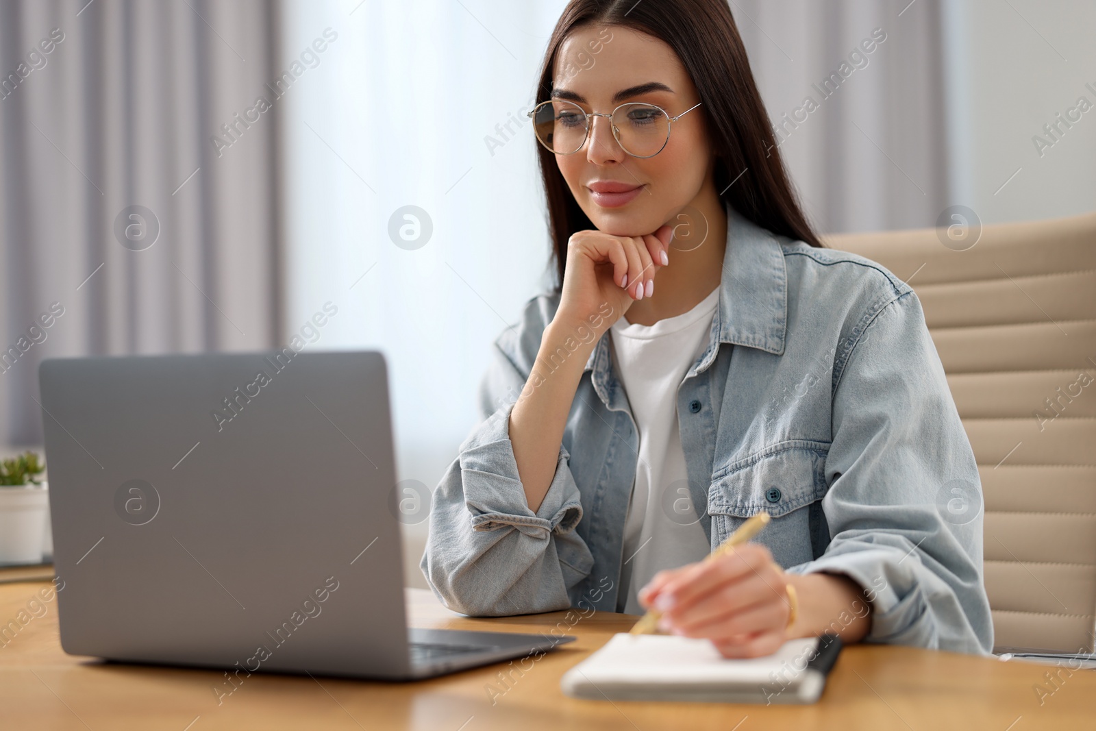 Photo of Young woman watching webinar at table in room