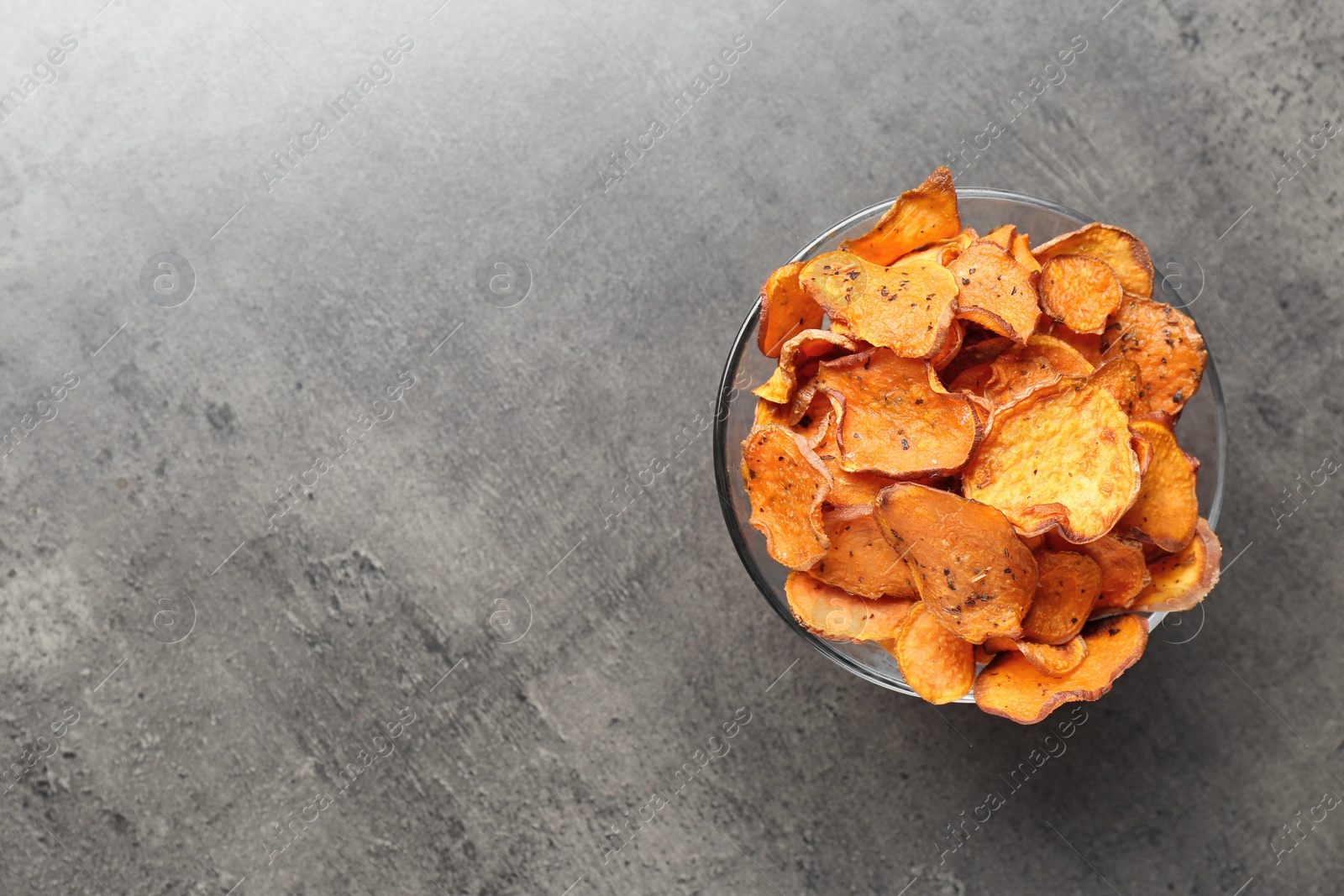 Photo of Bowl with sweet potato chips on grey table, top view. Space for text