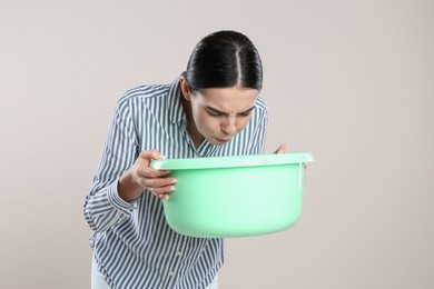 Woman with basin suffering from nausea on beige background. Food poisoning