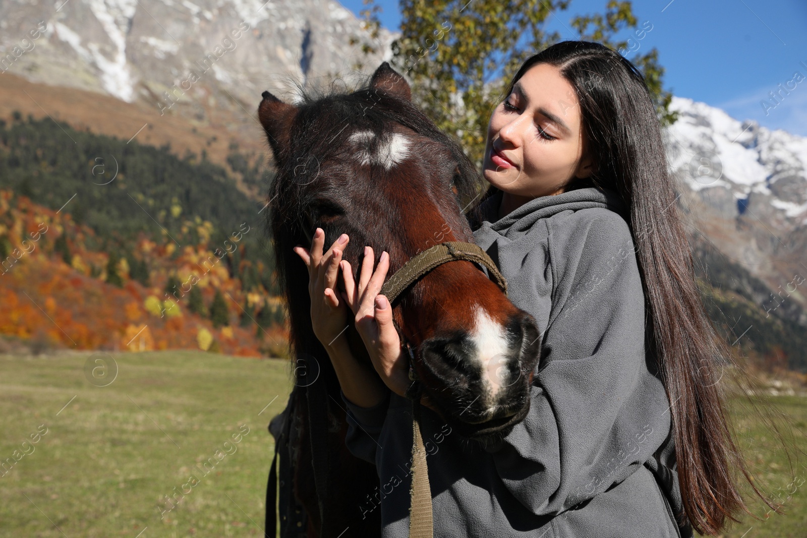 Photo of Young woman hugging horse in mountains on sunny day. Beautiful pet