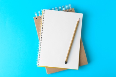 Notebooks with pencil on light blue background, top view