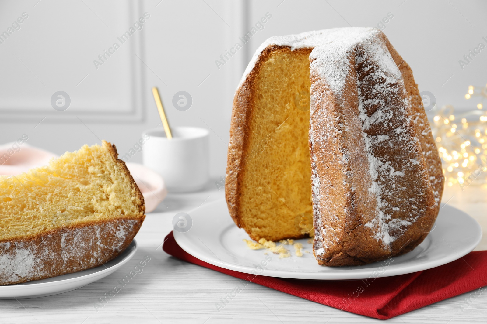 Photo of Delicious Pandoro cake decorated with powdered sugar on white wooden table. Traditional Italian pastry