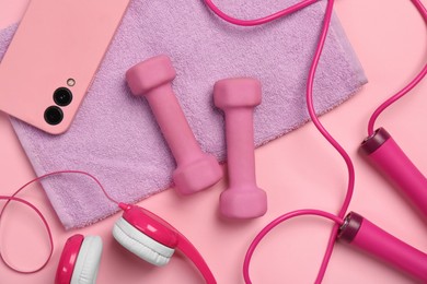 Flat lay composition with dumbbells and smartphone on pink background