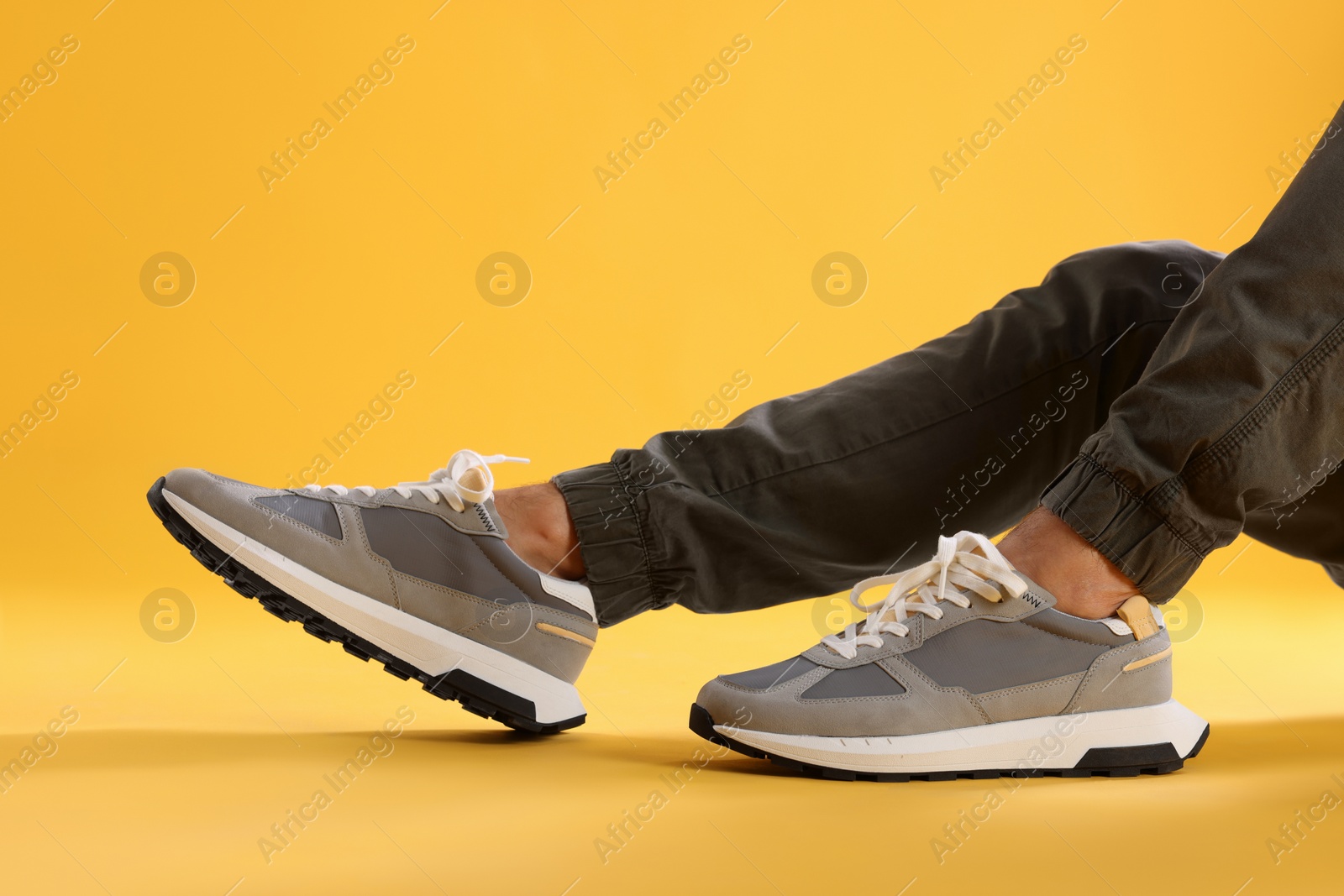 Photo of Man wearing stylish sneakers on yellow background, closeup