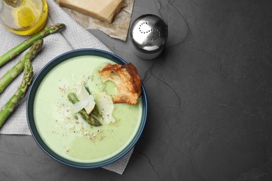 Photo of Bowl of delicious asparagus soup served on dark table, flat lay. Space for text