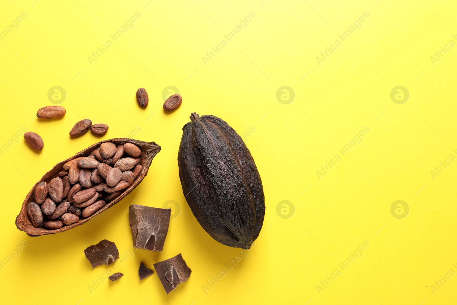 Photo of Cocoa pods with beans and chocolate pieces on yellow background, flat lay. Space for text